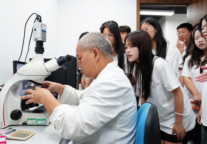 Man surrounded by university students looking into a microscope