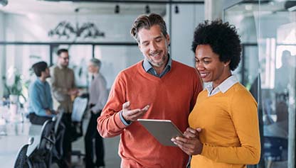 Two people smiling while looking at a tablet in an office environment